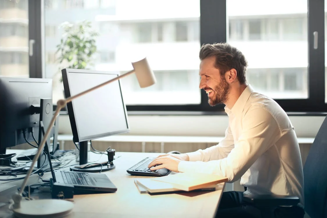 A smiling man working on a computer in a workplace