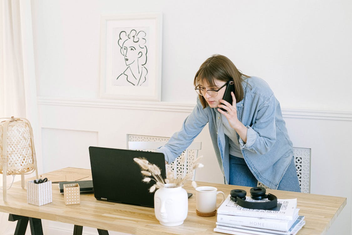 A person using a phone and a laptop simultaneously in a workspace