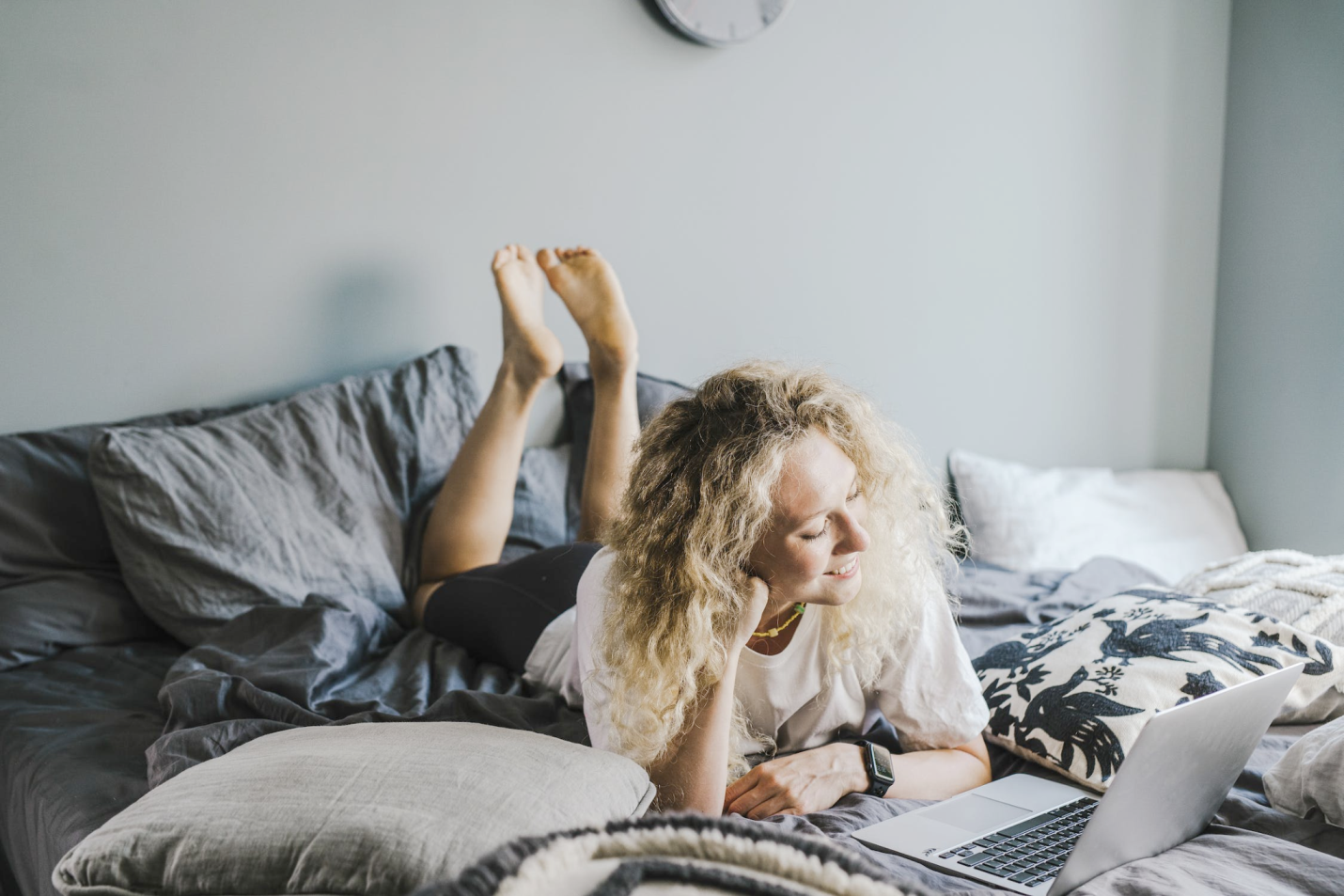 An image of a woman lying on the bed watching something on a laptop