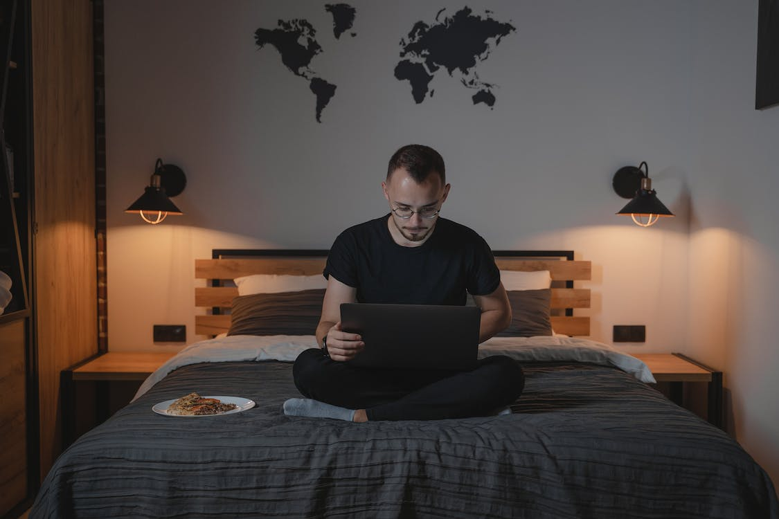 A man using his laptop while sitting on a bed