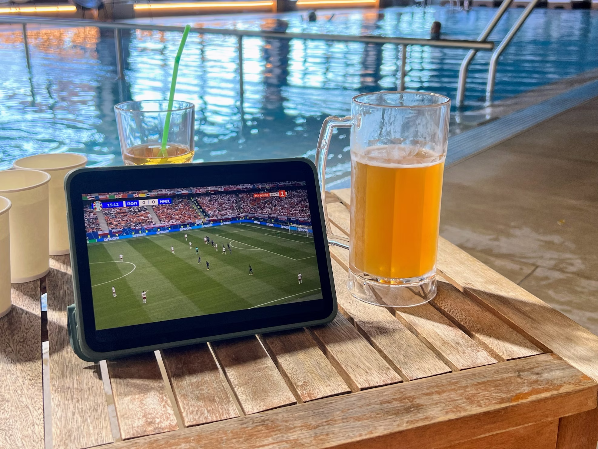 A person watching football on a tablet by a pool