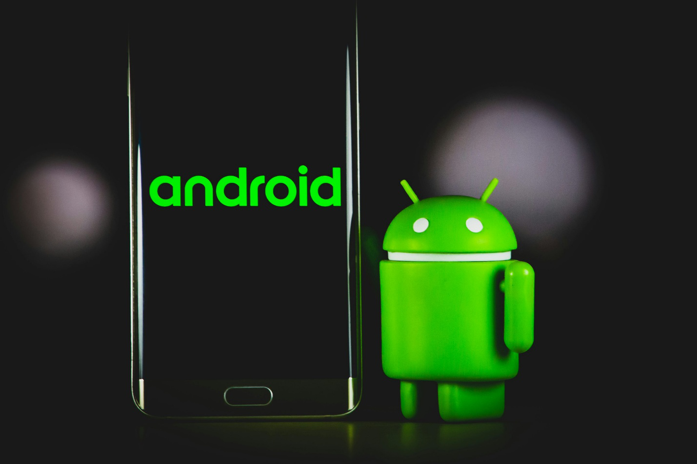 An Android phone next to a green Android figure