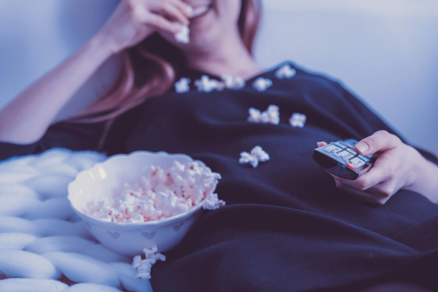  A woman eating popcorn with a remote in her hand 