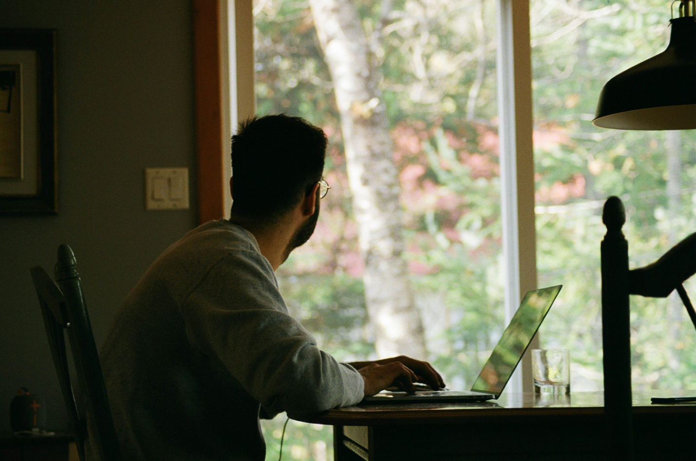 A man using a laptop and looking out a window