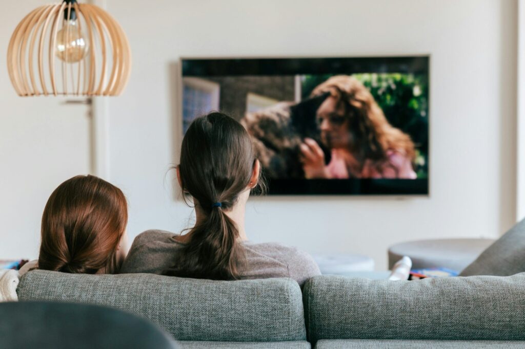 Two women sitting on a couch and watching TV