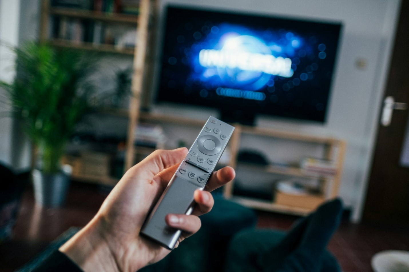 A person holding a gray remote up to a TV with a Universal Studios movie